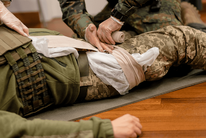 Military personnel applying a medical bandage to an injured leg during first aid training or emergency treatment.